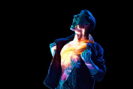 Burst of burning emotions. Expressive portrait of young emotional man shouting with digital space reflection on body in neon light. Concept of modern photography, art, cyberpunk, techno, creativity