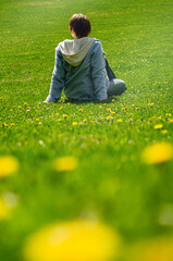 Girl in a meadow with green grass and dandelions on a sunny spring day