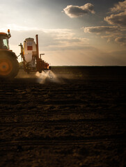 Tractor spraying land in sunset.