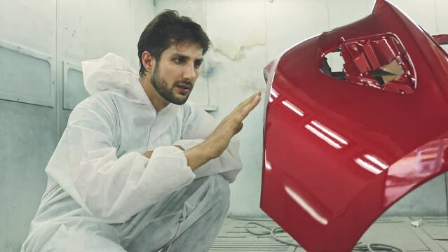 Skilled painter White uniform sits admiring the masterpiece painted red fiberglass front bumper of a restored car giving thumbs up in the paint room.