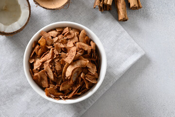 Coconut chips with cinnamon powder in bowl on gray background. Tasty sugar free snack. View from above. Copy space.