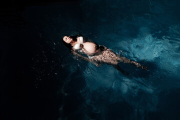 Fototapeta na wymiar Beautiful pregnant woman is swimming on water surface and enjoying.