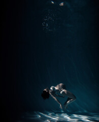 Naklejka na ściany i meble Underwater shoot of beautiful pregnant woman swimming in water through sunbeams.