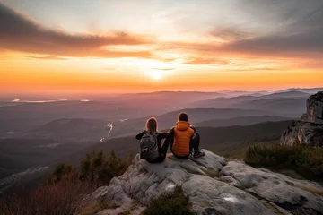 Zelfklevend Fotobehang A couple watching the sunset from a mountaintop, sitting, with a panoramic view of the surrounding landscape stretching out below them © Thilo