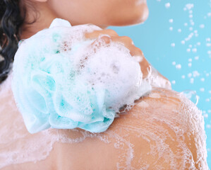 Fototapeta premium Use a loofah for a deeper clean. Studio shot of an unrecognizable young woman showering against a blue background.