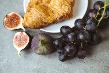 Autumn attributes. Croissant, dark grapes, book and figs on the grey table. Gold October