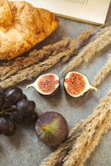 Autumn attributes. Croissant, dark grapes, book and figs on the grey table. Gold October