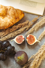 Autumn attributes. Croissant, dark grapes, book and figs on the grey table. Gold October