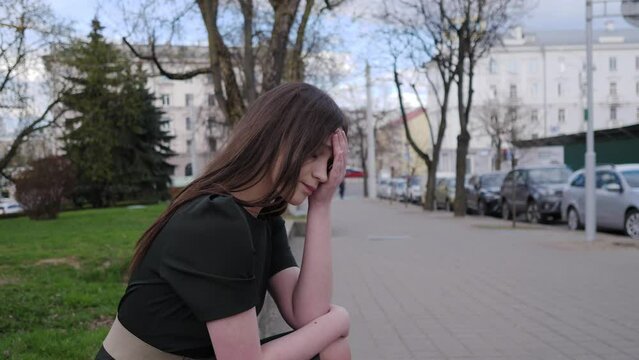 A sad beautiful girl sits on the curb on a city street