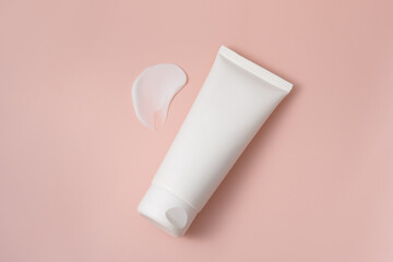 White blank tube of moisturizer or skin lotion with smear on pink isolated background. The concept of cosmetics, presentation or advertising of a new product