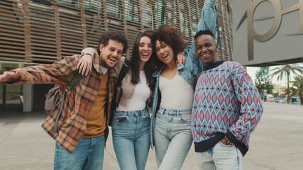 Close up, young smiling people posing while standing on the street. Four students look at the camera and smile.