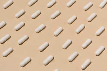 Pattern of white pills on a beige isolated background. The concept of pharmaceuticals, treatment for diseases and medical drugs
