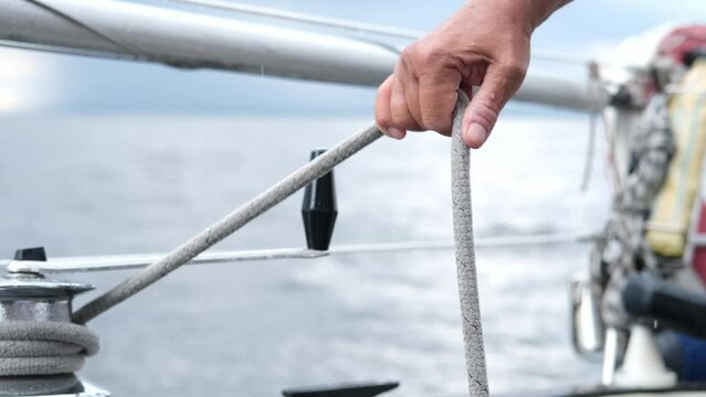 Close up of Yachtsman male hands holding rope on halyard winch of sailboat or on yacht