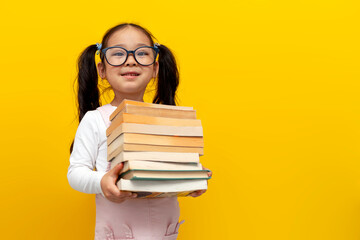 little asian girl with glasses holding books and smiling over yellow isolated background, korean...