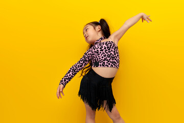 little asian girl in dance outfit dances chachacha on yellow isolated background, korean child...