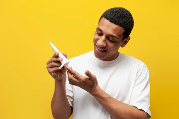 young african american guy in white t-shirt squeezes out cream from tube on yellow isolated background