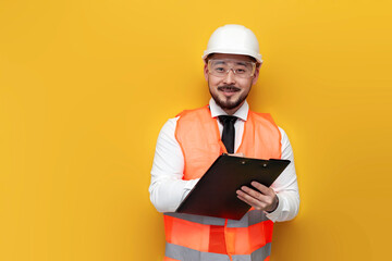 Asian civil engineer in uniform writes plan on paper and smiles on yellow isolated background