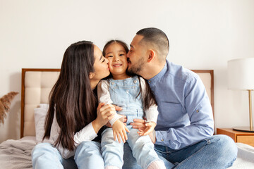 happy young asian family sit on bed together with daughter, korean little girl hug and love parents at home