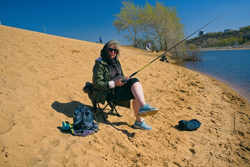 Fishing on the river by spinning. A woman is sitting on the riverbank with a fishing rod in her...