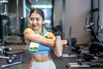 Fototapeta na wymiar Active young Asian woman stretching her body warm up before intensive workout at gym, basic gym exercises performed by the young female