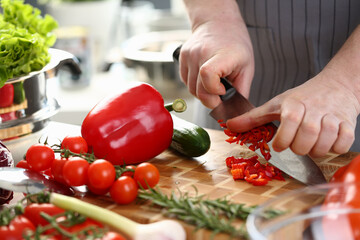 Closeup of a chef hands cutting vegetables on wooden table. Preparing vegetarian fresh vegetable salad in kitchen