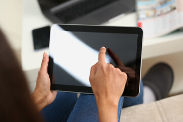 Woman hand holds tablet at home and controls finger across screen. Woman surfing internet using an app