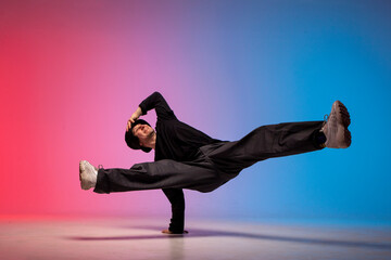 young guy dancer is dancing break in neon lighting, male acrobat is doing trick and dance exercise