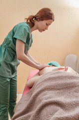Massage of the back of the scapula in salon. The masseuse massages the scapula of the lying client.
