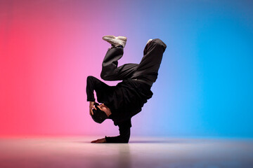 guy hiphop performer break dance in neon club lighting and doing acrobatic trick, male dancer stands in acrobatic pose
