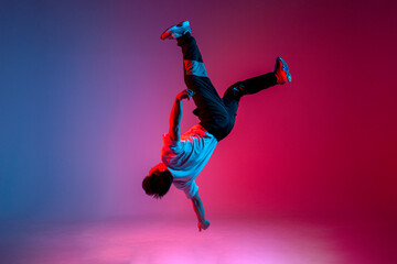 guy acrobat doing back fat in new lighting, male dancer jumps and falls in the air on red blue background - obrazy, fototapety, plakaty