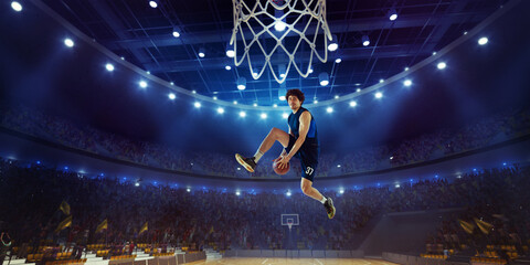 Young man, professional basketball player in motion, jumping with ball during match on 3D stadium...