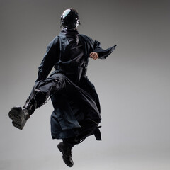 Urbantech outfit cyber style, a young man in stylish black clothes and a mirror mask on his whole face, in a jump. Studio photo on a light background