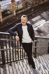 Smiling bestager man leaning on city stairs railing