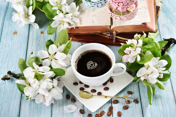 Spring apple blossoms and a cup of black coffee on blue wooden table