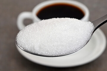 Cuillère de sucre en poudre en gros plan avec une tasse de café au second plan