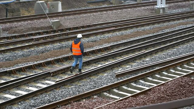 A man in work clothes is walking along the railroad tracks