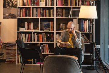 Young man alone escapes from the noise and obligations of marriage and work, sitting in a library or bookstore, reads a book in peace, calming his nerves and worries. Guy enjoys reading and studying © Srdjan