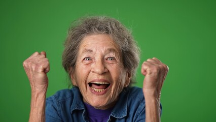 Closeup portrait of excited winner smiling elderly senior old woman with wrinkled skin and grey hair on green screen background.