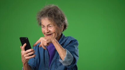Funny crazy elderly old toothless woman answering smart phone call say wow as winner with success pointing. Isolated on green screen background.