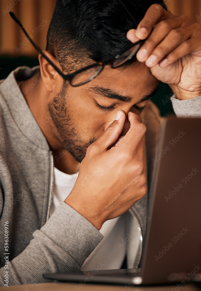 Poster Closeup of young indian man feeling stressed while sitting alone and using a laptop to browse the internet. Mixed race student suffering from a headache while studying late at night. Making mistakes