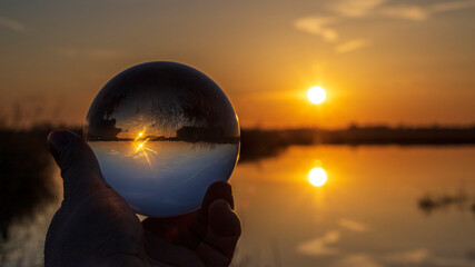 Glaskugel im Moor bei Sonnenuntergang. Durch die Spiegelung im Wasser und die Reflexion in der Kugel sind gleich vier Sonnen zu sehen.