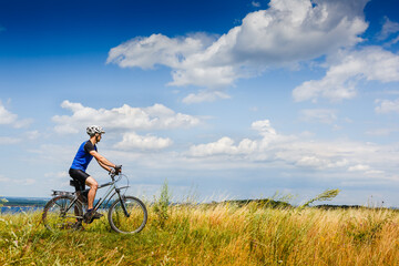 Fototapeta na wymiar young athletic man on a bicycle riding the green meadow trail on sunny day