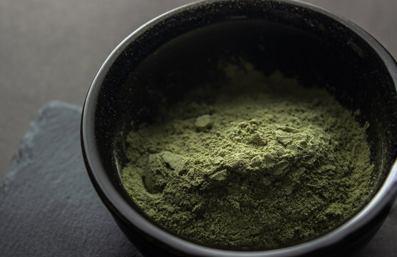 Green powder in a small ceramic bowl, on a stone stand, on a black background.  Super food or marijuana kief concept