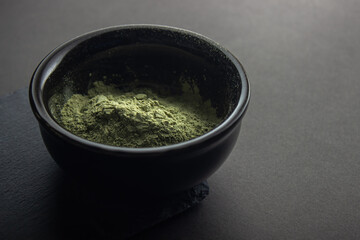 Green powder in a small ceramic bowl,  on a black background.  Super food or marijuana kief concept