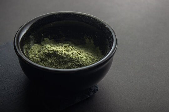 Green powder in a small ceramic bowl,  on a black background.  Super food or marijuana kief concept