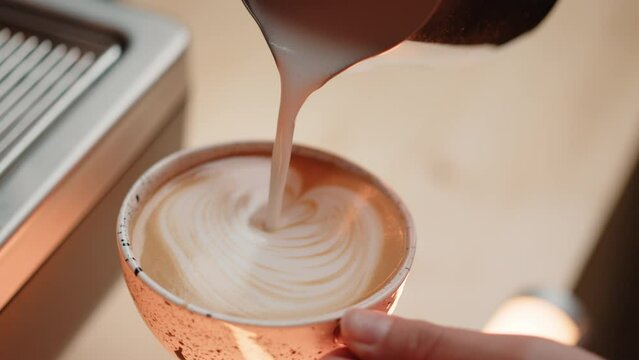 Pouring foamed milk into a beautiful cup of coffee. The barista prepares a delicious cappuccino at the bar. Pleasant warm atmosphere of the cafe