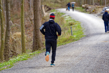 Male jogger with cap on gravel pathway in the woods on a cloudy spring day. Photo taken April 7th, 2023, Zurich, Switzerland.