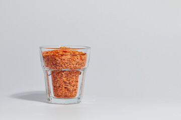 Lens culinaris is scientific name of Turkish Red Lentil legume. Also known as Lentilha Vermelha (portuguese). Top view of grains in a glass. White and blue background.