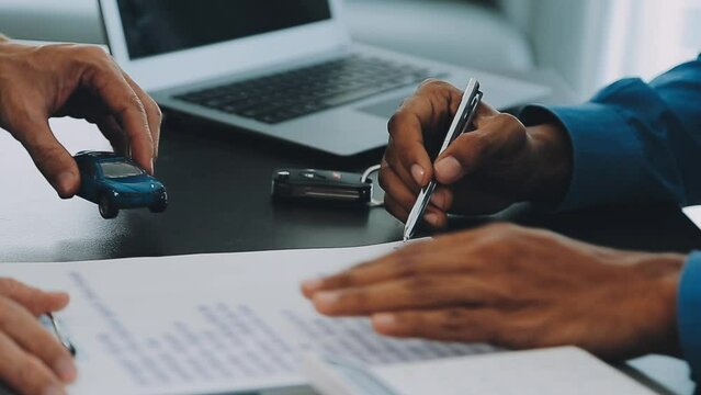 Closeup of Asian female signing car insurance document or lease paper contract or agreement. Buying or selling new or used vehicle with car keys on table.
