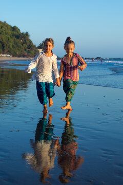 Two young hippie girls run along the ocean beach.
